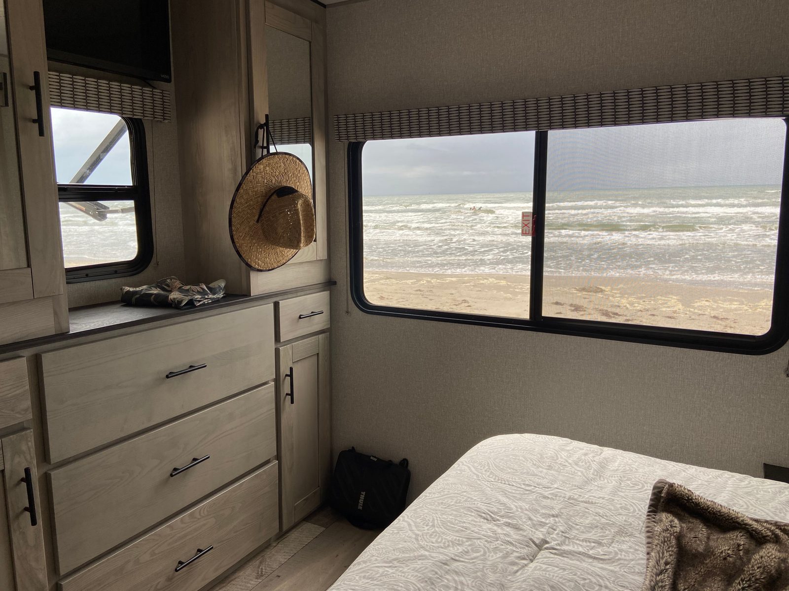 Made up bed in a camper bedroom next to a window and a small dresser