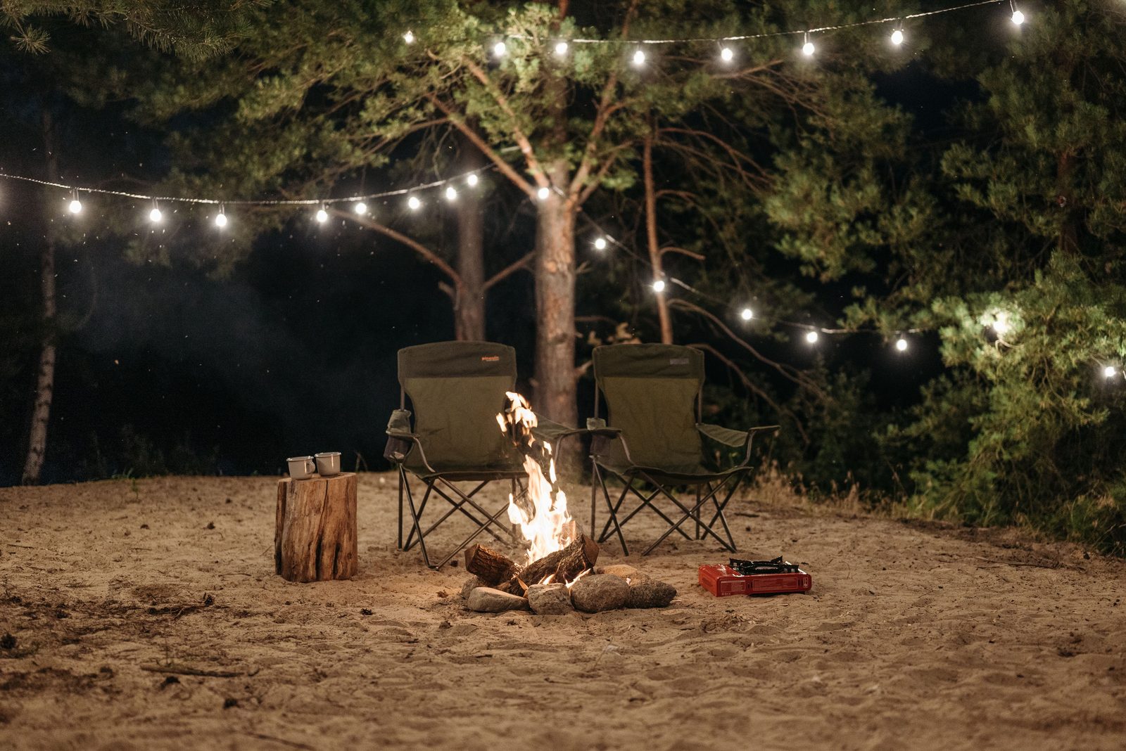 Camp chairs around a fire at night under a strand of warm white string lights