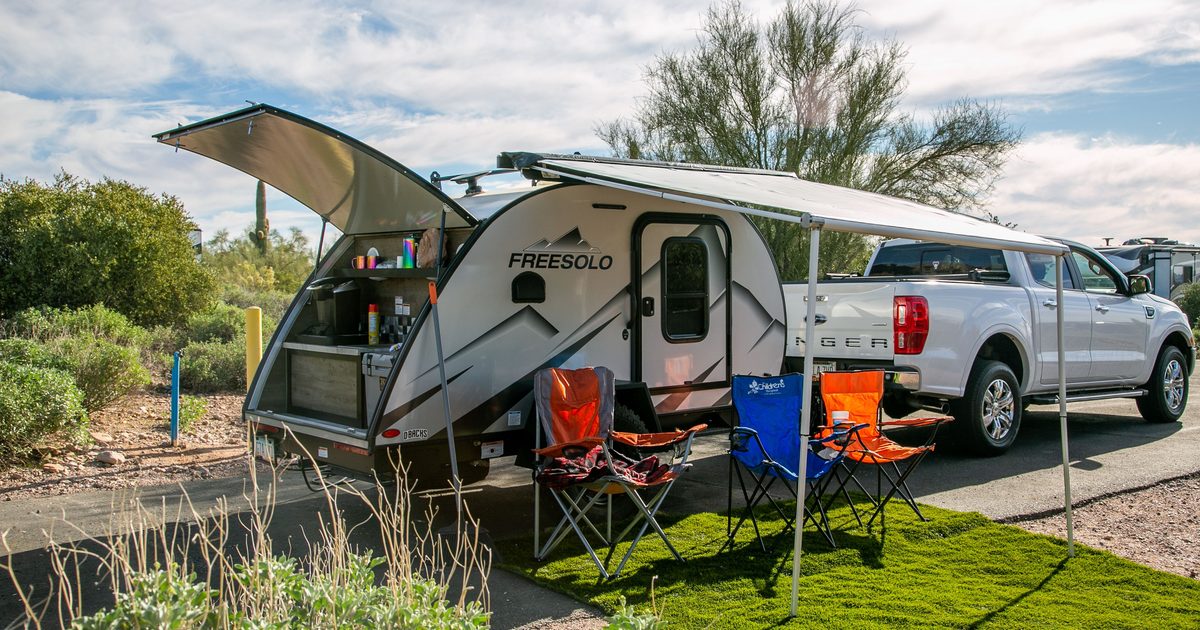 Teardrop camper parked next to a truck with the awning out, camp chairs and an outdoor rug set up