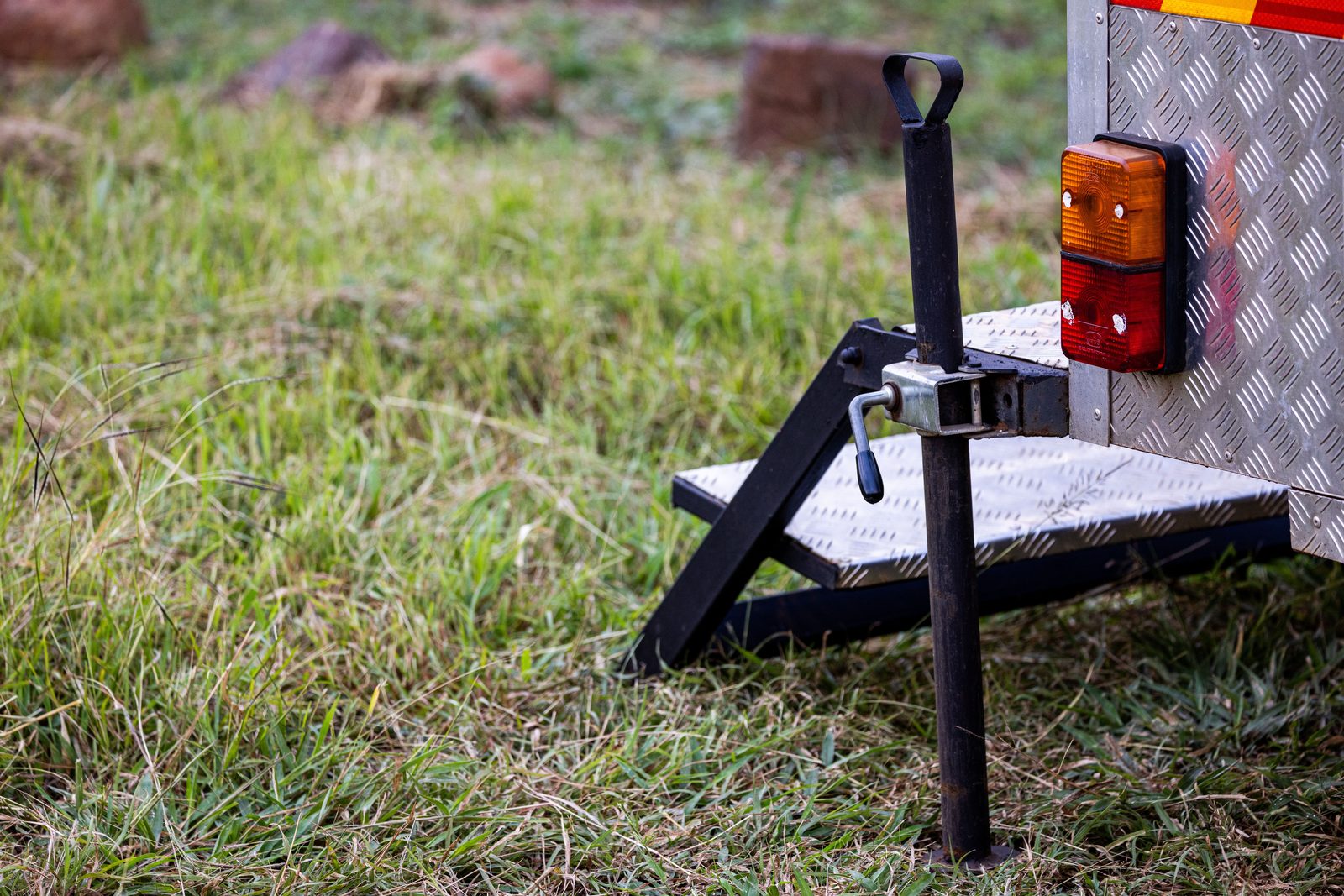 Trailer stabilizer jack cranked down onto a leveling pad in the grass