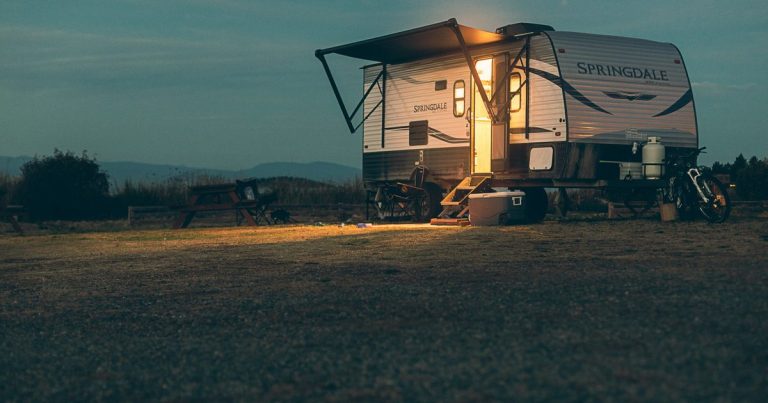 Travel trailer parked in an open field at dusk with the awning out and lights on