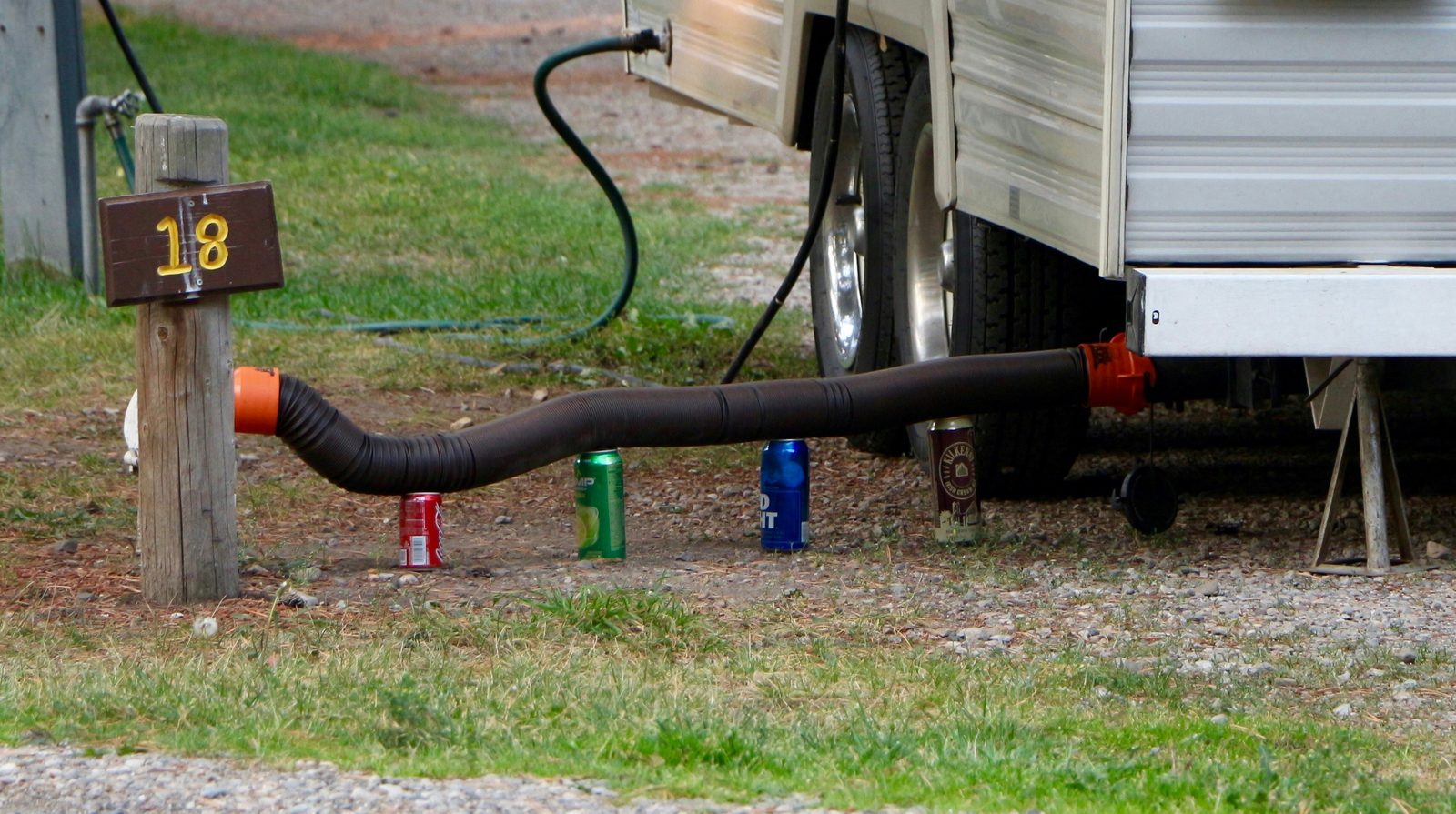 Sewer hose and leveling blocks connected to a travel trailer at a campsite hookup post