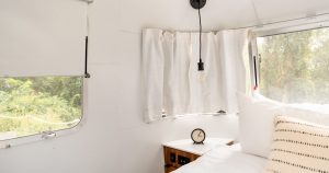 Bright white camper bedroom interior with a made bed, curved RV windows and blank walls ready for wallpaper